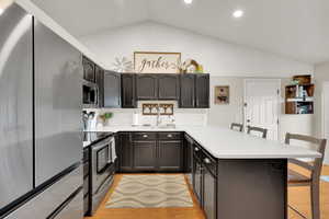Kitchen featuring a peninsula, a kitchen bar, a sink, appliances with stainless steel finishes, and vaulted ceiling