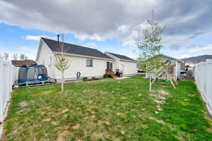 Back of house with a playground, a trampoline, a lawn, and a fenced backyard