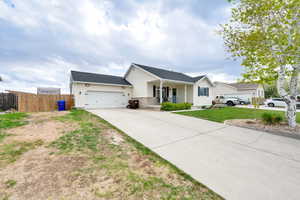 Single story home with a front lawn, fence, covered porch, an attached garage, and driveway