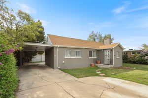 Ranch-style home with a chimney, stucco siding, an attached carport, a front lawn, and concrete driveway