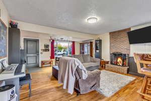Living room with a brick fireplace, light wood finished floors, and a textured ceiling