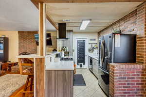 Kitchen featuring visible vents, freestanding refrigerator, brick wall, light countertops, and island exhaust hood