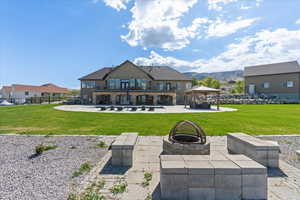 Rear view of property featuring a gazebo, a patio area, a balcony, a lawn, and a fire pit