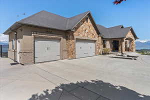 View of front facade featuring driveway, a garage, a mountain view, a shingled roof, and stone siding