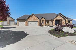 View of front facade with brick siding, driveway, stone siding, and a garage