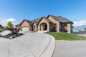 French country inspired facade featuring fence, a front lawn, stone siding, a garage, and curved driveway