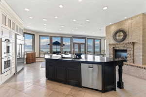Kitchen featuring a kitchen island with sink, a fireplace, dark cabinetry, a sink, and stainless steel appliances