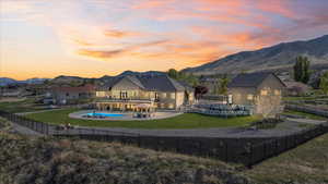 Back of house at dusk featuring a fenced in pool, a mountain view, a balcony, a fenced backyard, and a yard