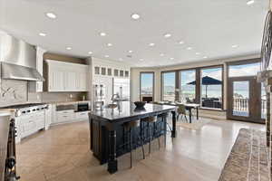 Kitchen featuring backsplash, a kitchen bar, a sink, built in appliances, and wall chimney exhaust hood
