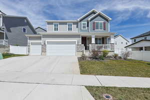 Craftsman house featuring fence, stone siding, a porch, a front yard, and concrete driveway