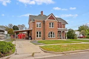 View of front facade featuring a storage unit, brick siding, a front yard, an outbuilding, and a balcony