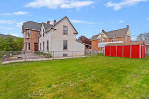 Back of property with a storage shed, fence, an outbuilding, and a yard