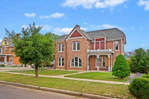 View of front of house featuring brick siding, a chimney, a shingled roof, and a front yard
