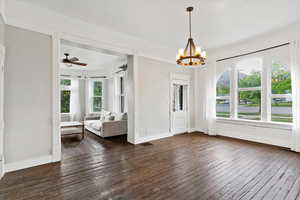 Unfurnished dining area with visible vents, dark wood finished floors, ceiling fan with notable chandelier, and baseboards
