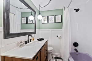 Bathroom featuring wainscoting, a decorative wall, vanity, toilet, and shower / tub combo