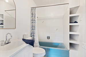 Bathroom featuring vanity, shower / bathtub combination with curtain, and toilet