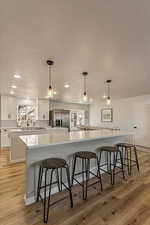 Kitchen with stainless steel fridge, a sink, light wood finished floors, backsplash, and a spacious island
