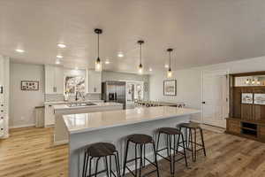 Kitchen featuring a large island, a kitchen breakfast bar, stainless steel fridge, tasteful backsplash, and light wood-style flooring