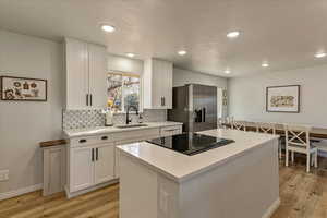 Kitchen featuring a sink, stainless steel fridge with ice dispenser, stovetop with downdraft, and light wood-style flooring