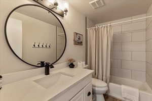 Full bathroom with visible vents, shower / bath combination with curtain, toilet, and vanity