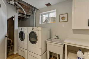 Clothes washing area with light wood-style floors, laundry area, a sink, and washer and clothes dryer