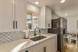 Kitchen with appliances with stainless steel finishes, a sink, light countertops, white cabinetry, and backsplash