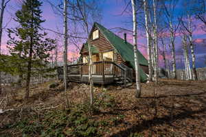 Back of property at dusk with a wooden deck, log veneer siding, and metal roof