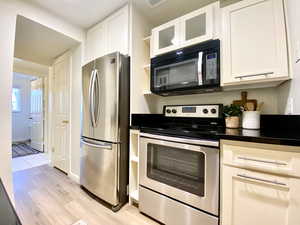 Kitchen featuring dark countertops, appliances with stainless steel finishes, light wood-style flooring, and white cabinetry