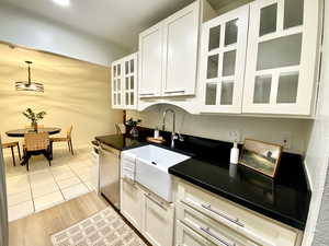 Kitchen with decorative light fixtures, dark countertops, stainless steel dishwasher, a sink, and white cabinets