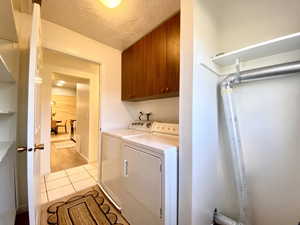 Clothes washing area featuring a textured ceiling, cabinet space, light tile patterned floors, and washer and dryer