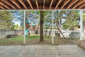 View of patio with a playground and a fenced backyard