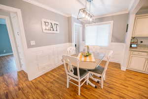 Dining area with crown molding, a decorative wall, light wood-type flooring, and a wainscoted wall