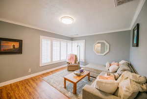 Living area with a textured ceiling, ornamental molding, wood finished floors, and visible vents
