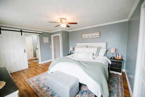 Bedroom featuring ceiling fan, a barn door, wood finished floors, baseboards, and ornamental molding
