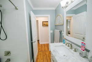 Bathroom with crown molding, vanity, shower / bathtub combination, wood finished floors, and baseboards