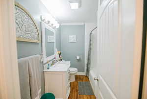 Bathroom featuring crown molding, vanity, toilet, shower / bathtub combination with curtain, and wood finished floors