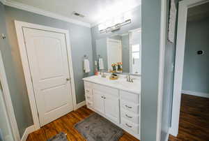 Full bathroom with a sink, ornamental molding, wood finished floors, and visible vents