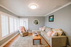 Living room with a textured ceiling, visible vents, crown molding, wood finished floors, and baseboards