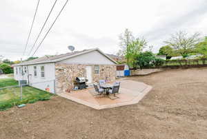 Rear view of house featuring fence, stone siding, a shed, central AC unit, and a patio area