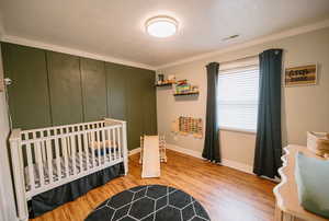 Bedroom featuring crown molding, baseboards, visible vents, and wood finished floors