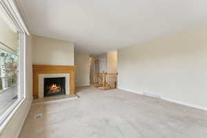 Unfurnished living room featuring baseboards, a fireplace, carpet flooring, and visible vents