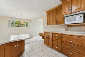 Kitchen featuring light countertops, white microwave, brown cabinetry, and light carpet