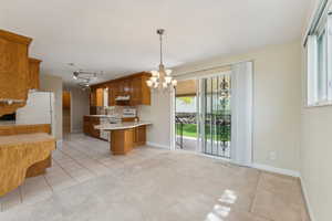 Kitchen featuring brown cabinets, an inviting chandelier, light countertops, a peninsula, and light tile patterned floors