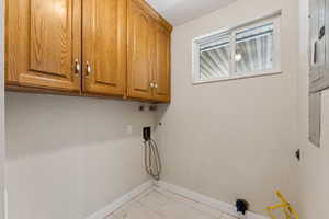 Clothes washing area featuring cabinet space, light tile patterned floors, baseboards, and washer hookup