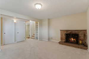 Unfurnished living room with a textured ceiling, a fireplace, stairway, carpet floors, and baseboards