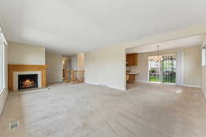 Unfurnished living room featuring a lit fireplace, a notable chandelier, visible vents, and baseboards