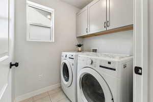 Clothes washing area featuring cabinet space, separate washer and dryer, baseboards, and light tile patterned flooring