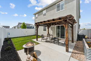 Rear view of house featuring a fenced backyard, a patio, stucco siding, and an outdoor fire pit