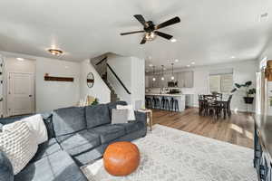 Living room with stairway, ceiling fan, light wood-type flooring, and visible vents