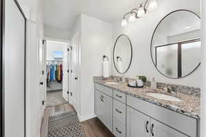 Primary bathroom with wood finished floors, double vanity, a sink, and a stall shower